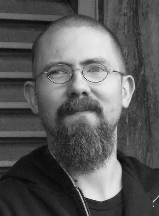 Portraifoto Felix Stoever, Schwarz weiß, Brille und Bart, schaut nach links vor Holzwand