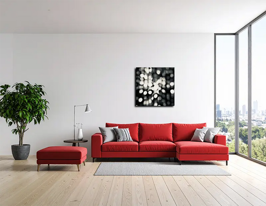 Das abstrakte quadratische Foto hängt an einer hellen wand hinter  einem roten Sofa und einem Fenster von rechts 
