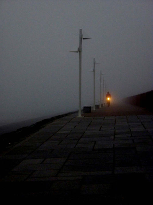 ein Radfahrer fährt in der Dunkelheit auf dem Deich, die Lampe des Rades leuchtet