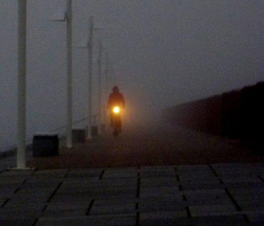 ein Radfahrer fährt in der Dunkelheit auf dem Deich, die Lampe des Rades leuchtet, detailaufnahme