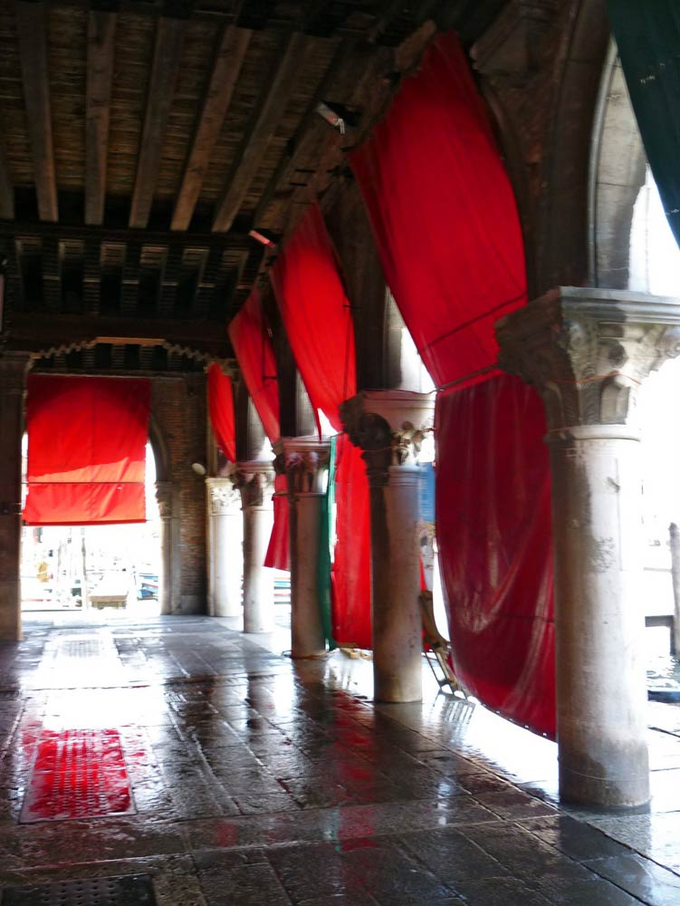 Ein Torgang in Venedig, Säulen und rote Tücher im Sonnenschein